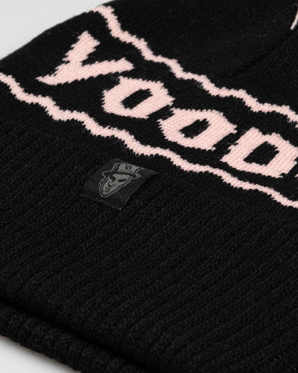 Black beanie with pink text and a brand logo on a light gray background