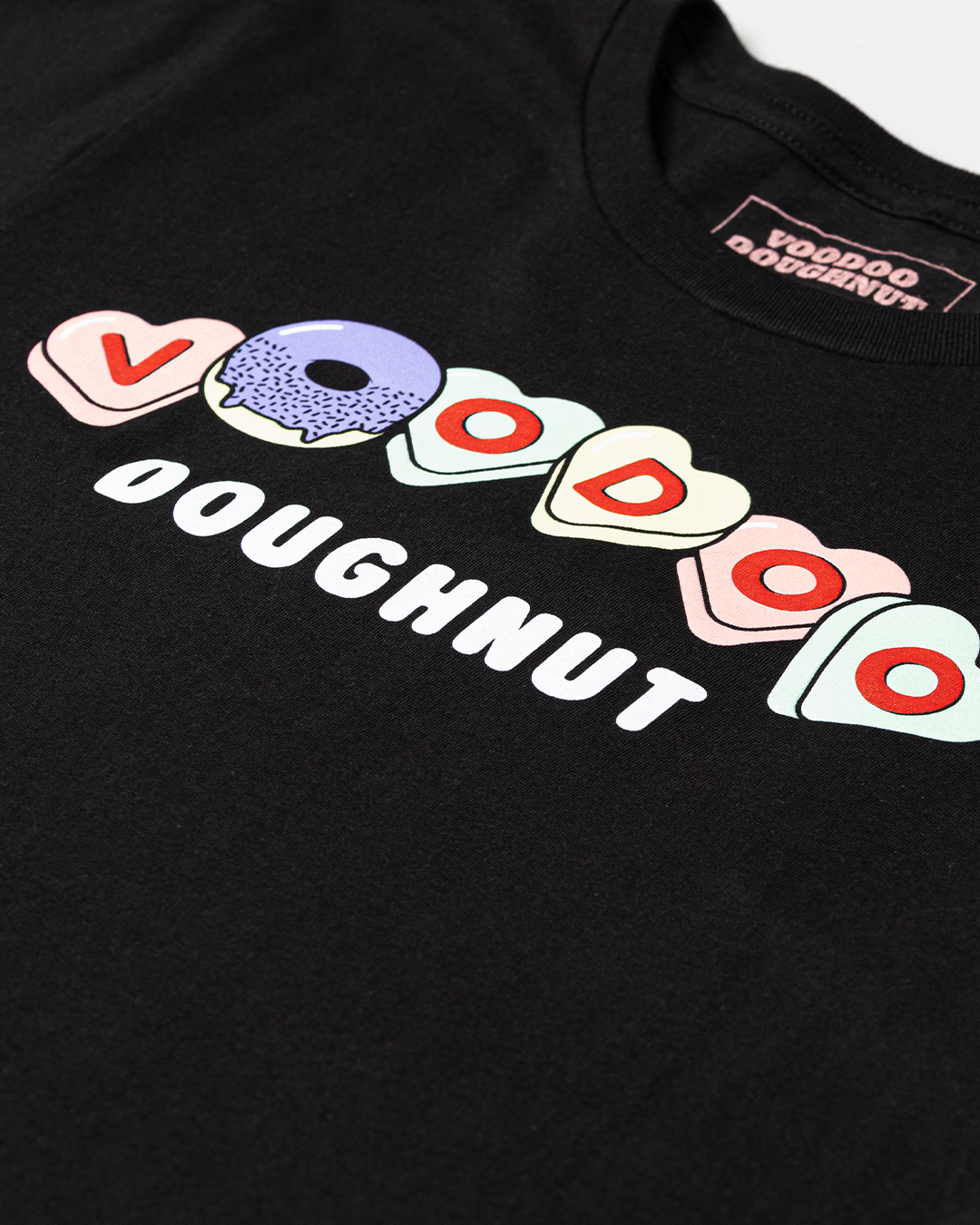 Close up of Black t-shirt with colorful heart designs and text "Voodoo Doughnut" on the hearts